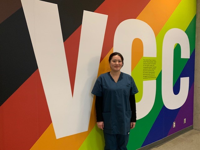 Supportive Care Assistant student in scrubs by a wall that says VCC