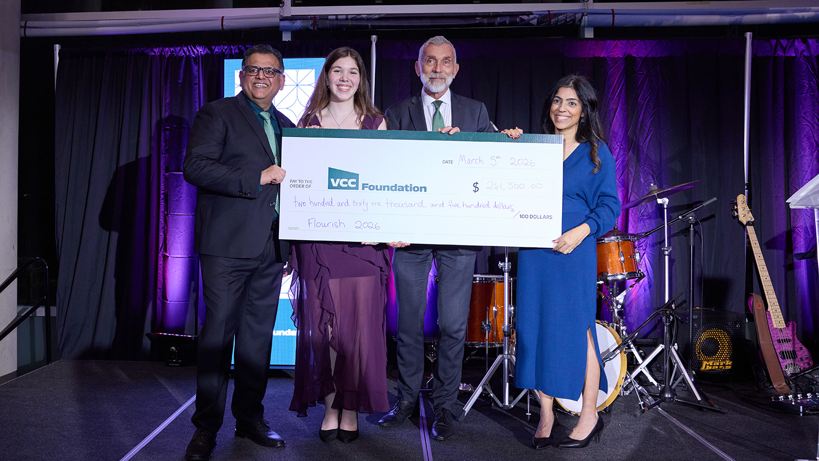 Four people present an oversized cheque on stage