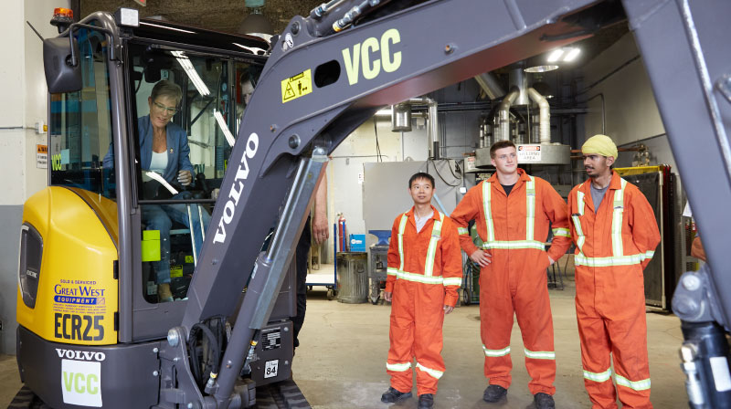 Minister Robinson in an excavator while VCC students look on