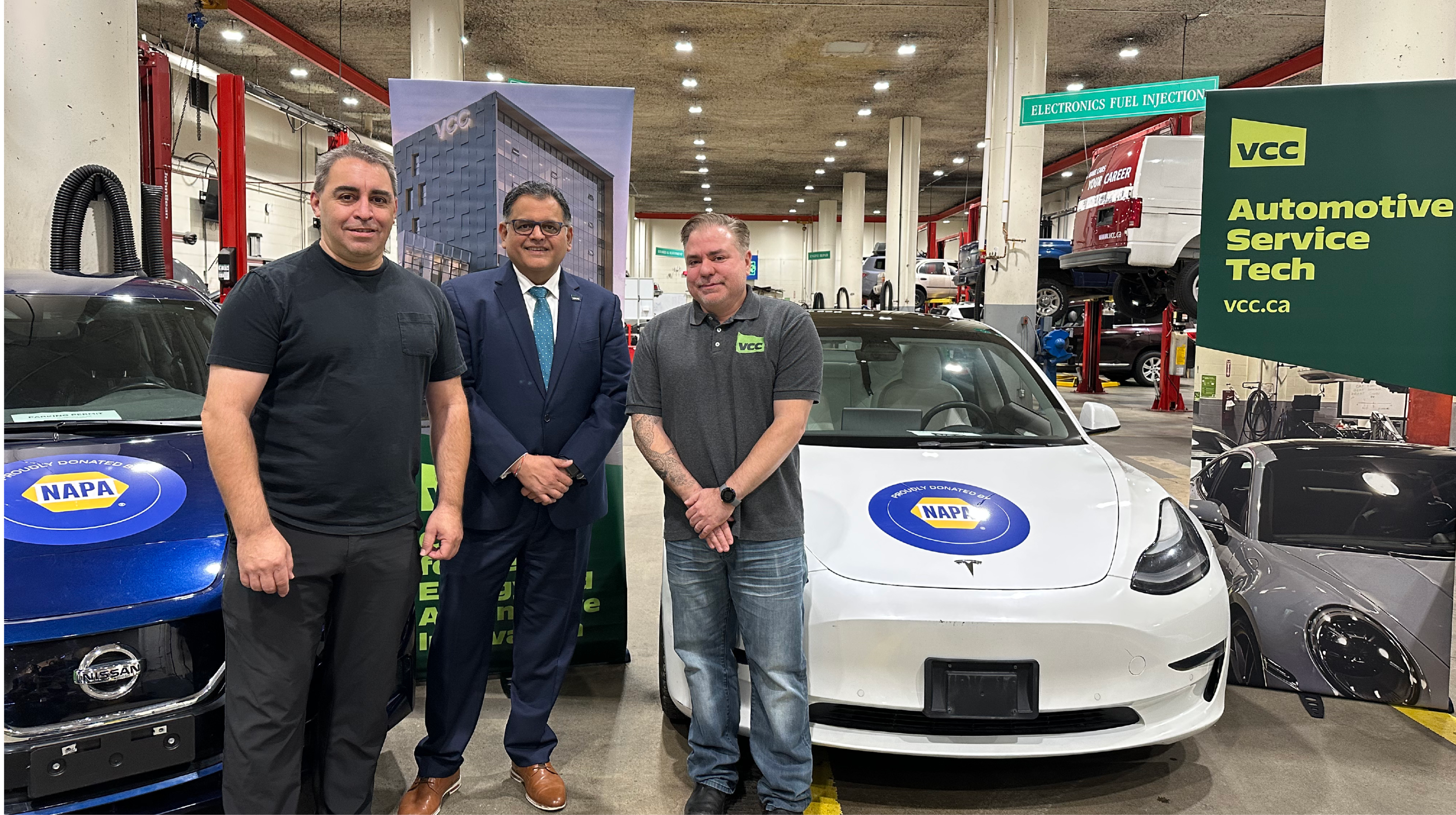 Three men pose in front of electric vehicles in an auto bay
