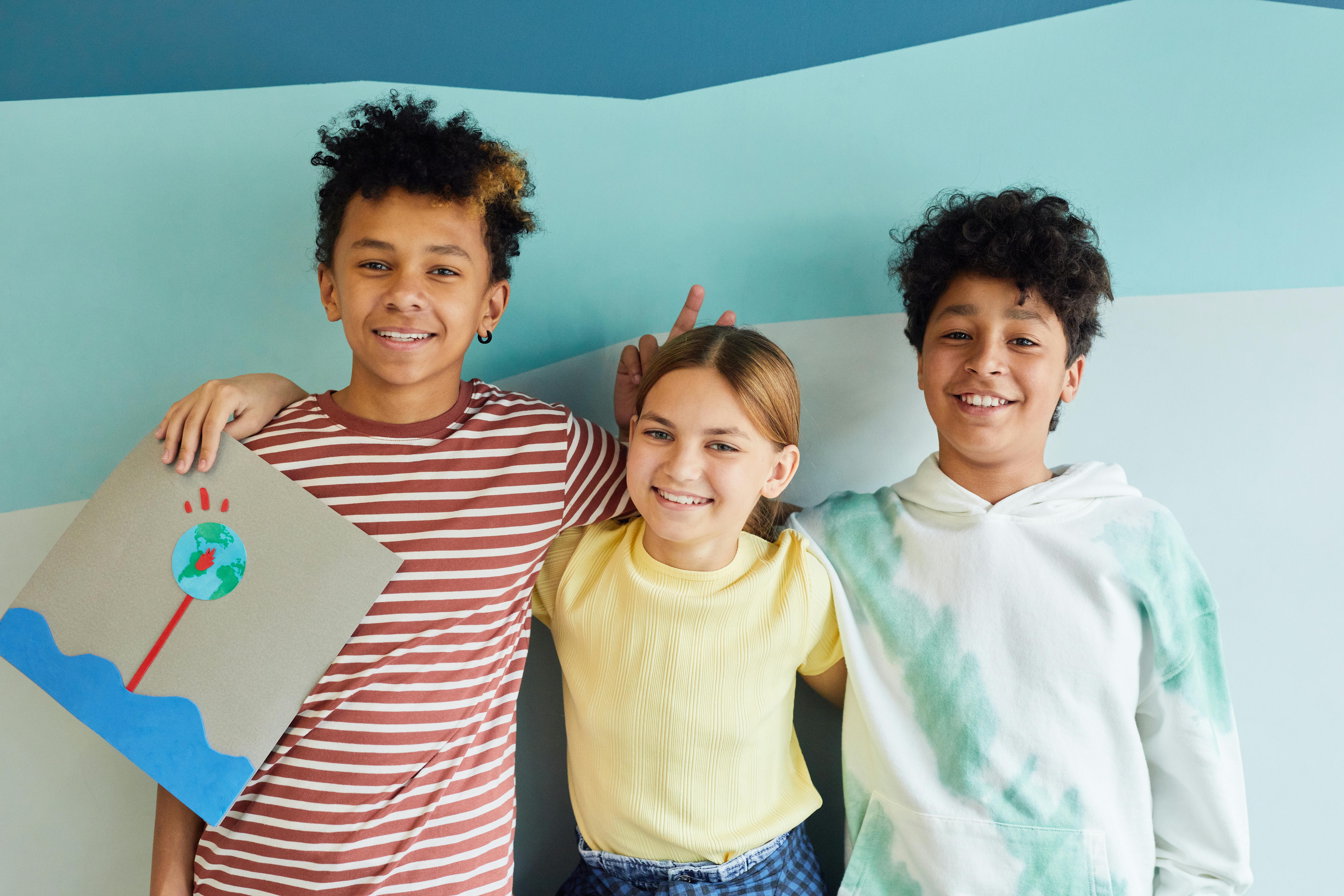 A girl holding a painting and two boys, smiling and posing to the camera