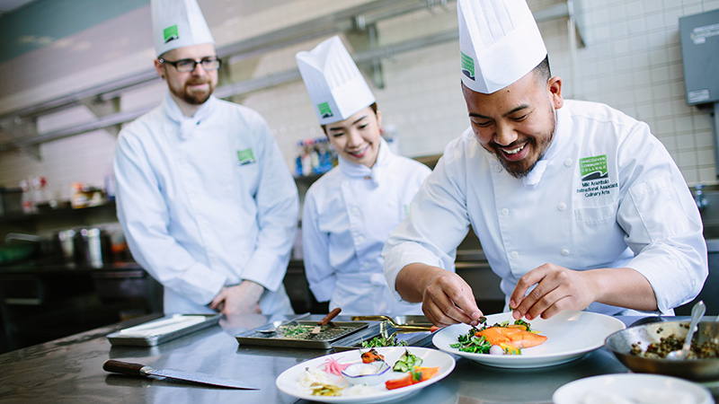 A culinary instructor demonstrates plating salmon to two students