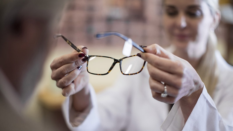 Optician helping a patient try on glasses
