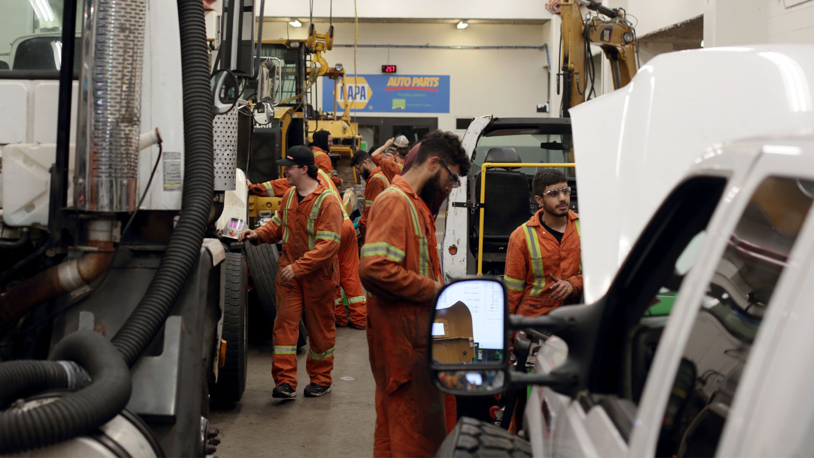 Heavy mechanical trade apprentices are actively working on large trucks.