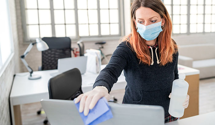 woman wearing a mask is wiping the computers clean with disinfectant