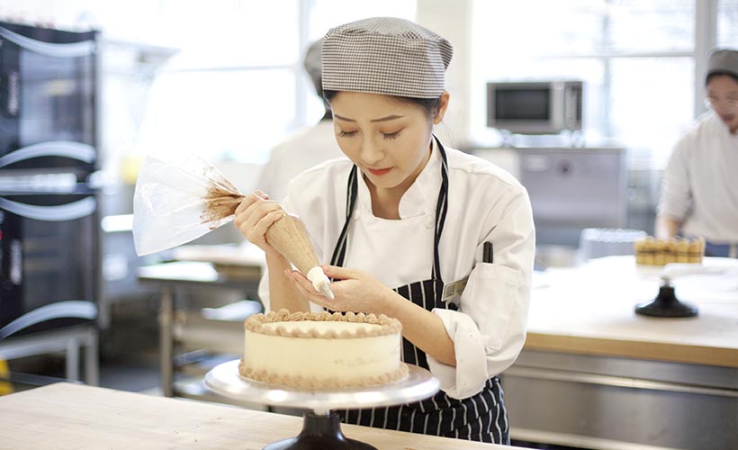 Female student in classroom, decorating a cake