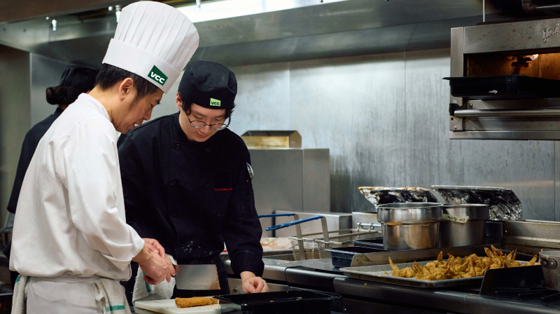 Asian Culinary arts instructor demonstrating a cooking technique to a student