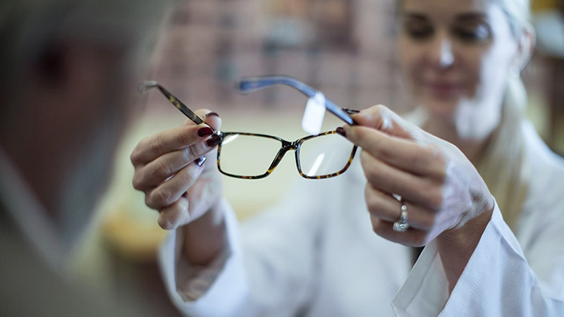An optician student holds out eye glasses to try on.